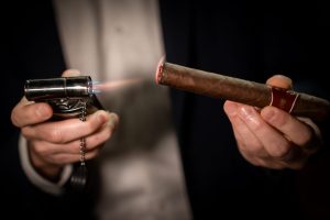 Prim-plan cu trabuc aprins, cu flacără și fum delicat, pregătit pentru a fi fumat, ideal pentru începătorii în lumea trabucurilor.