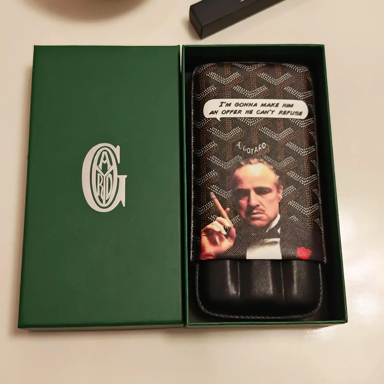 Etui pentru telefon The Godfather așezat în cutia sa, cu capacul scos și pus lângă.